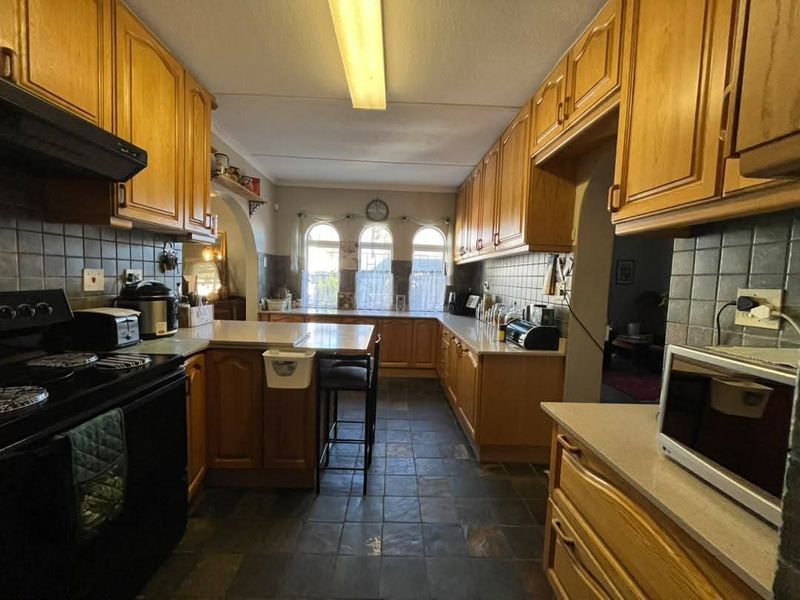 A traditional kitchen featuring wooden cabinetry, tiled backsplash, stone countertops, and a functional layout with an integrated oven and extractor fan.
