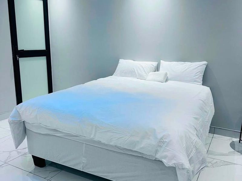 A modern bedroom featuring sleek tiled flooring, recessed ceiling lighting, and a contemporary frosted glass door.