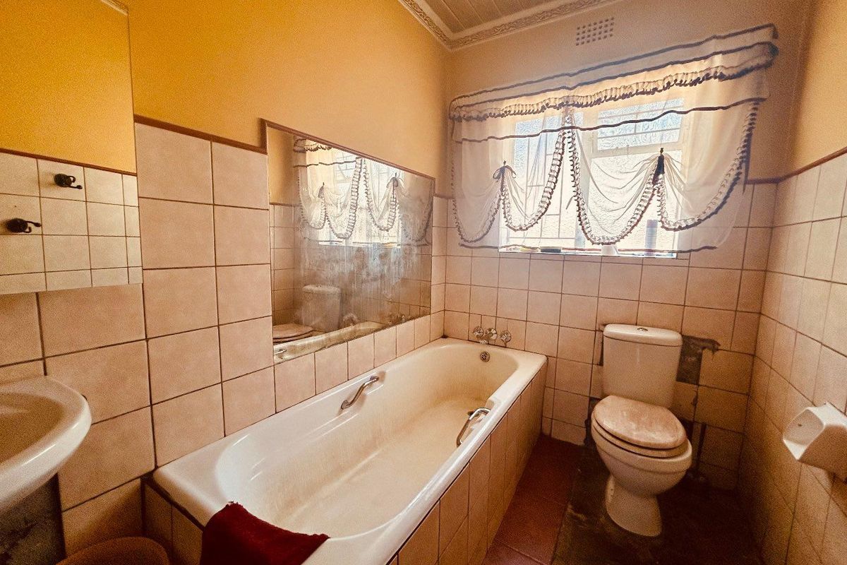 A dated bathroom featuring a built-in bathtub, wall-mounted basin, and toilet, with original tiling and classic ceiling cornice detailing.