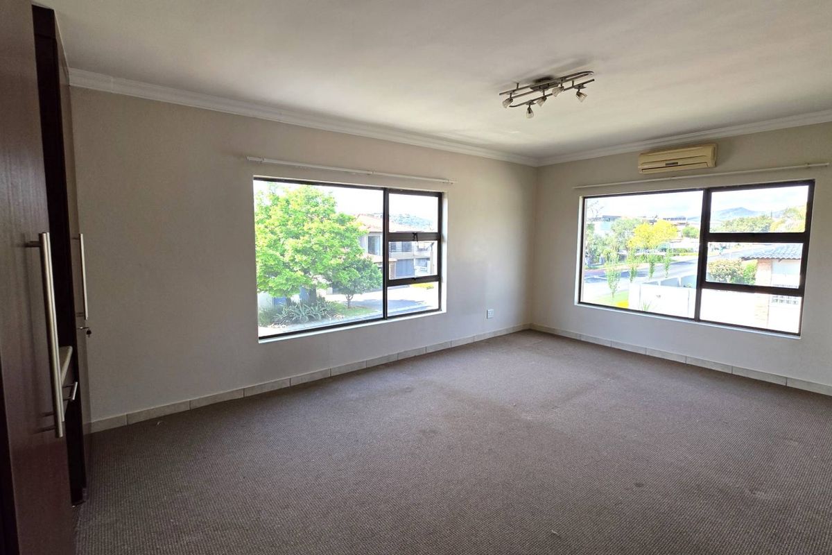 A spacious, empty bedroom featuring built-in cupboards, wall-to-wall carpeting, and large windows providing natural light and neighbourhood views.