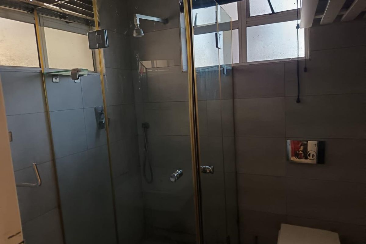 A functional bathroom featuring a glass-enclosed shower, wall-mounted toilet, and tiled walls with natural light from high-level windows.