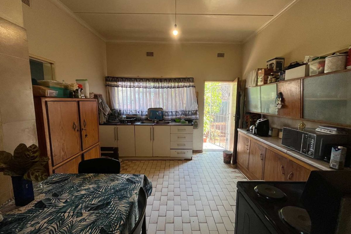 A functional kitchen featuring built-in wooden cabinetry, tiled flooring, and direct access to the rear exterior area.