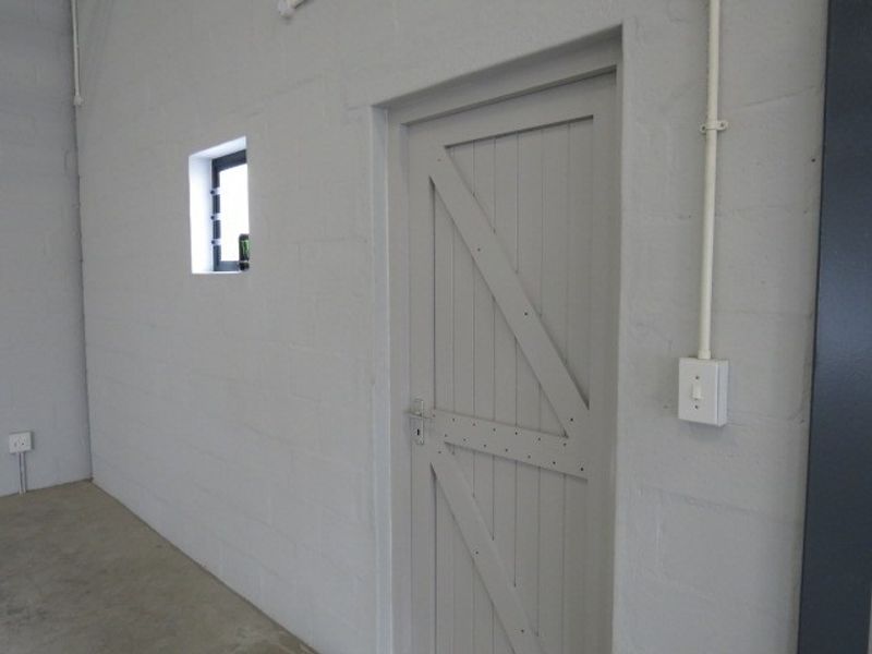 A clean, functional utility space featuring painted brick walls, exposed electrical conduit, a timber braced door, and durable concrete flooring.