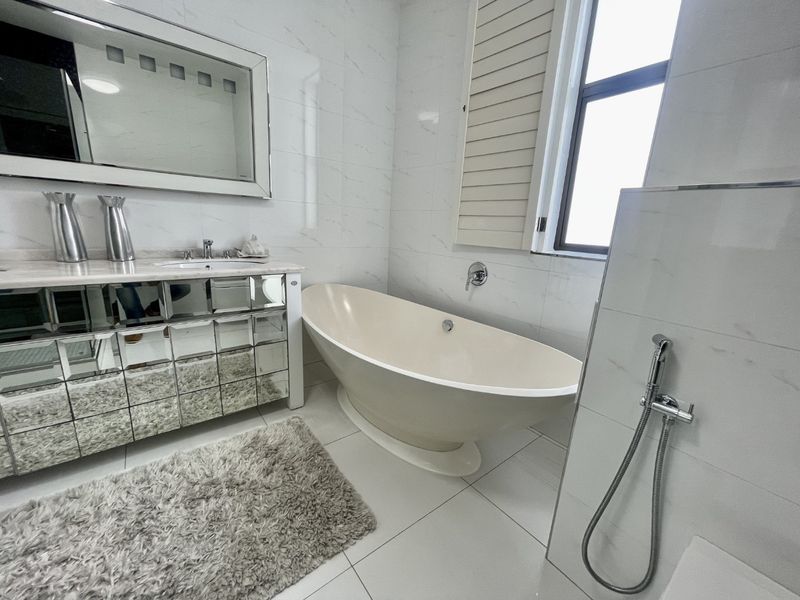 Modern bathroom featuring a sleek freestanding bathtub, a mirrored vanity unit, and elegant marble-look wall tiling with plantation shutters for natural light.