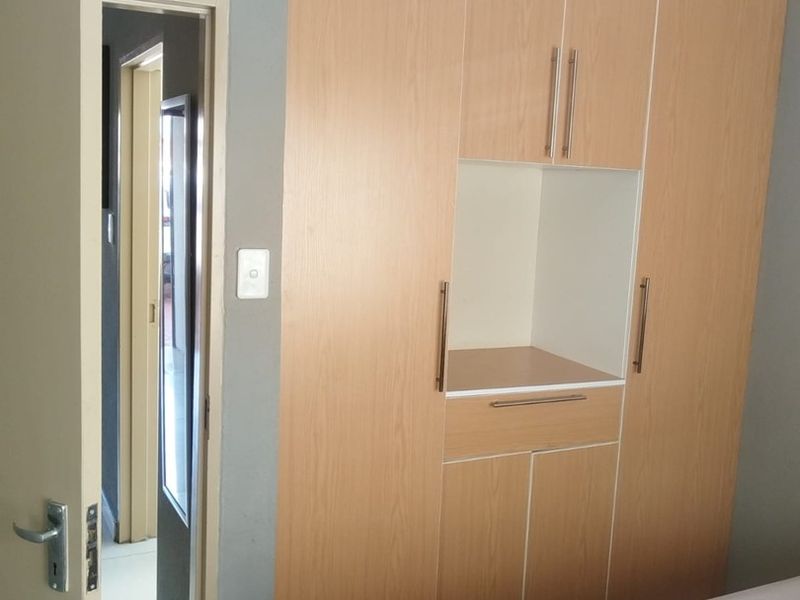 A bedroom featuring light wood-finish built-in cupboards with integrated shelving and a neutral grey wall finish.