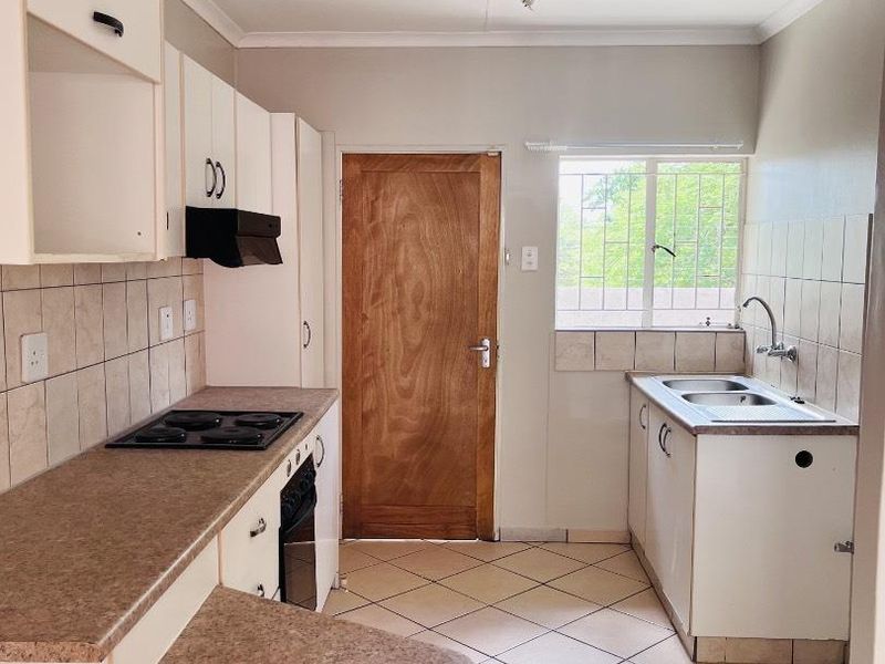 A functional kitchen featuring built-in cabinetry, laminate countertops, an electric hob, oven, and a double sink with tiled splashbacks and flooring.