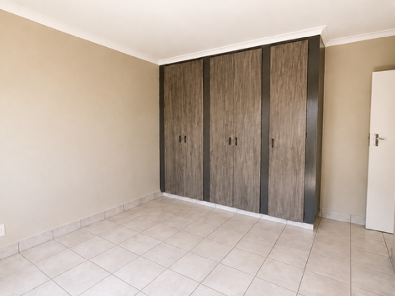 A clean, empty bedroom featuring neutral wall tones, tiled flooring, and modern wood-finish built-in cupboards.