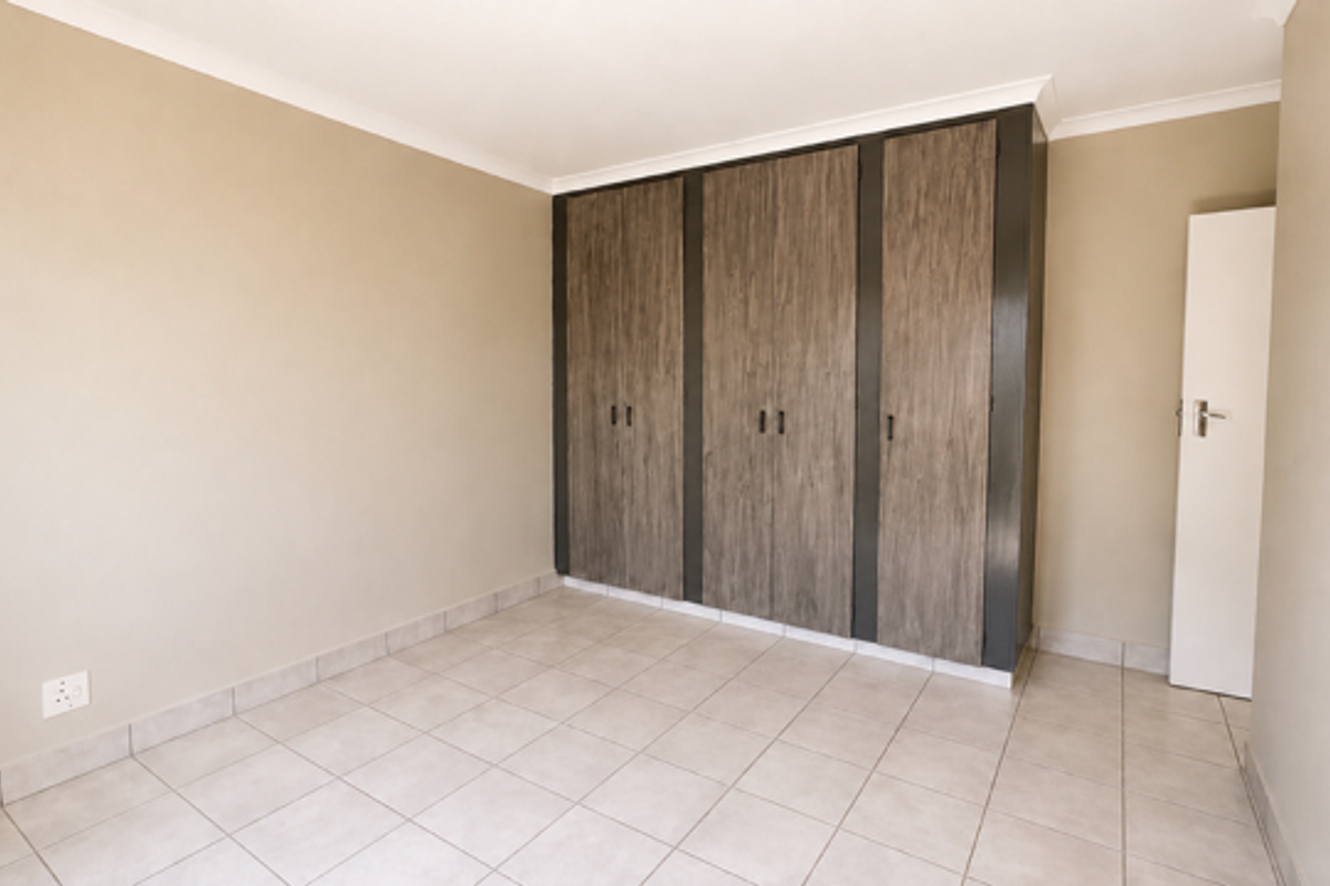 A clean, empty bedroom featuring neutral wall tones, tiled flooring, and modern wood-finish built-in cupboards.