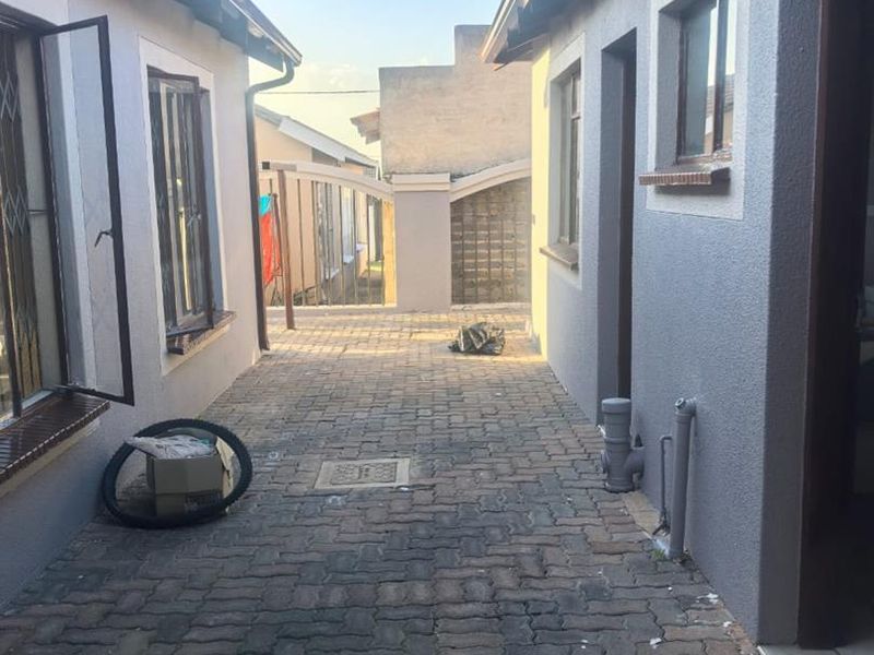 A paved side walkway between two sections of the house, featuring exterior wall finishes, drainage access, and security bars on the windows.