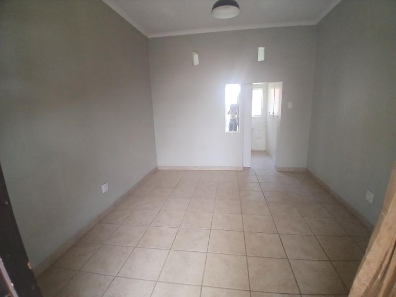 An empty, neutral-toned living area featuring ceramic floor tiles, built-in storage, and direct access to an adjacent room.