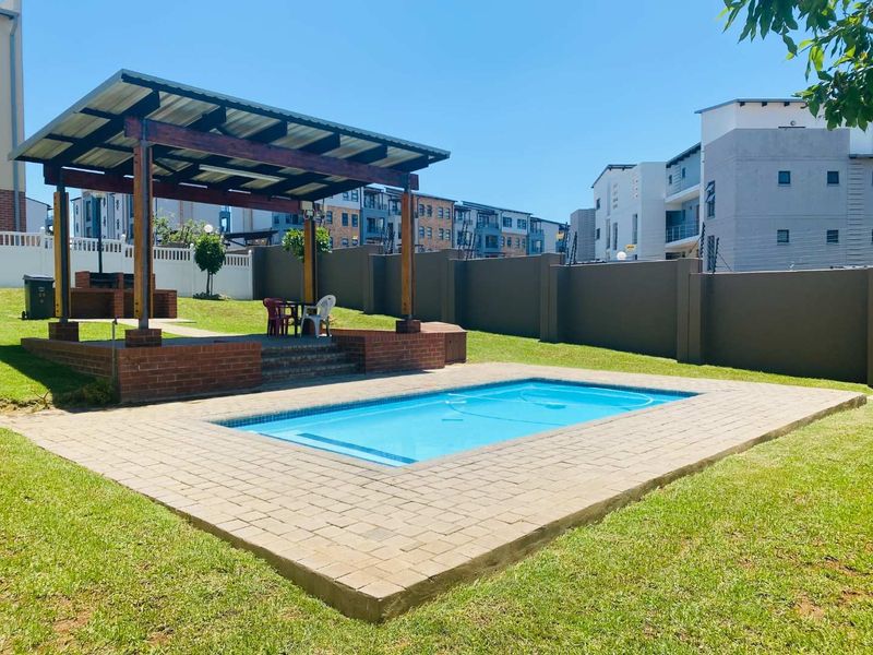 Outdoor pool area featuring a swimming pool with brick paving, a covered patio structure, and a built-in brick braai, set within a private garden.