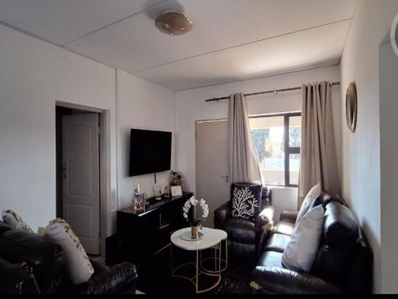 A functional living room featuring neutral walls, a window with curtain treatments, and access to adjacent rooms via internal doors.