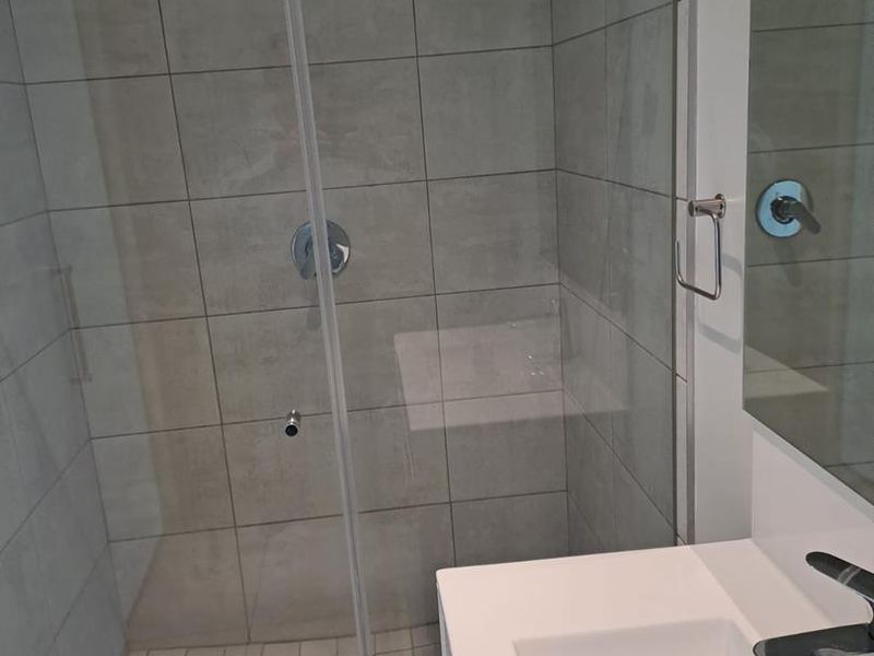 Modern bathroom featuring a glass-enclosed shower with neutral wall tiling and a clean vanity basin with chrome fixtures.