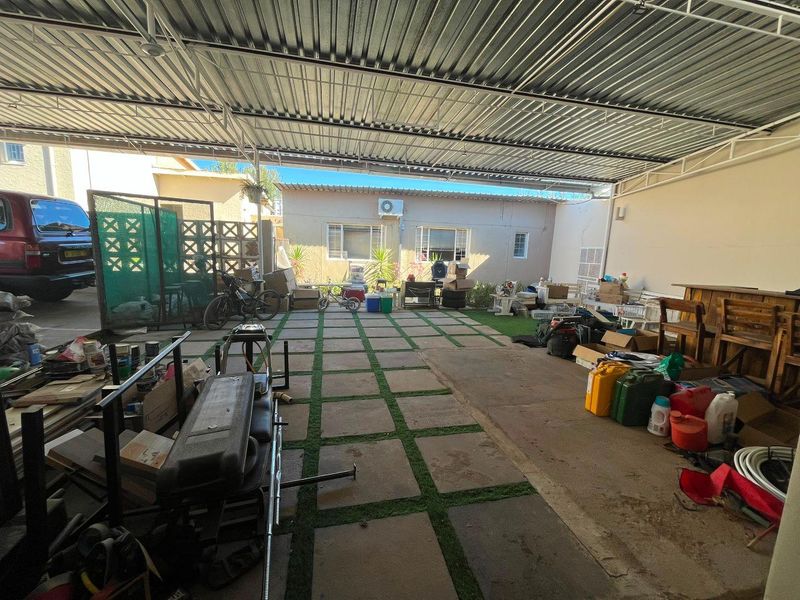 A large covered outdoor patio area featuring a corrugated metal roof and paved flooring with artificial grass accents, suitable for outdoor entertaining.