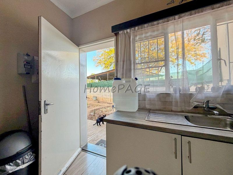 A functional scullery area featuring built-in cabinetry, a stainless steel sink, and direct access to the rear exterior.