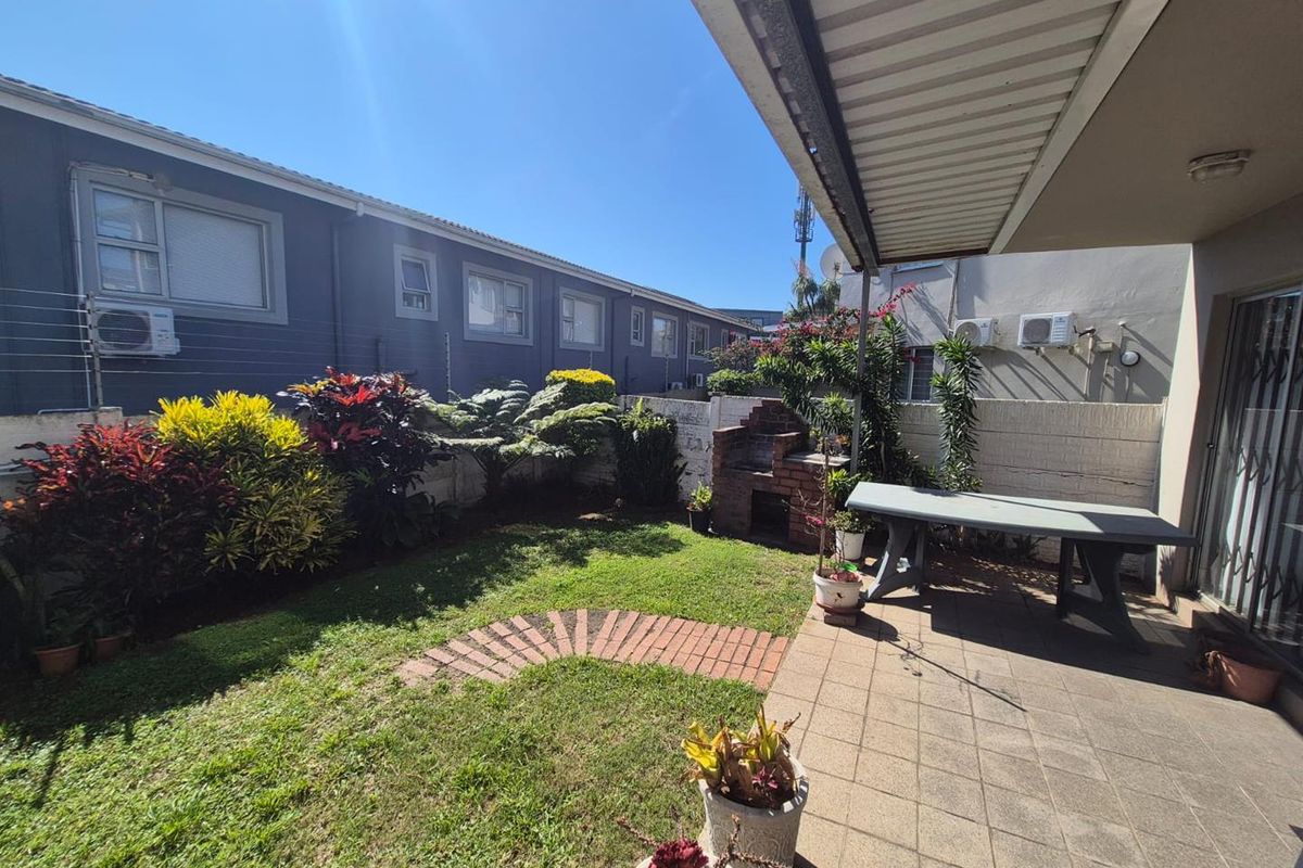 A private rear garden featuring a paved patio area with a built-in brick braai, lawn, and perimeter wall with electric fencing.