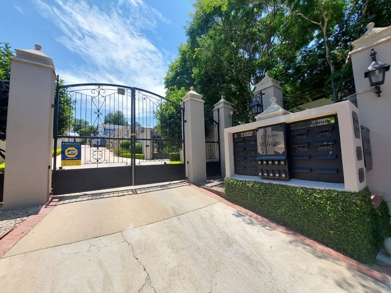Secure gated entrance to Orion Village featuring a wrought iron gate, concrete driveway, and integrated post boxes.