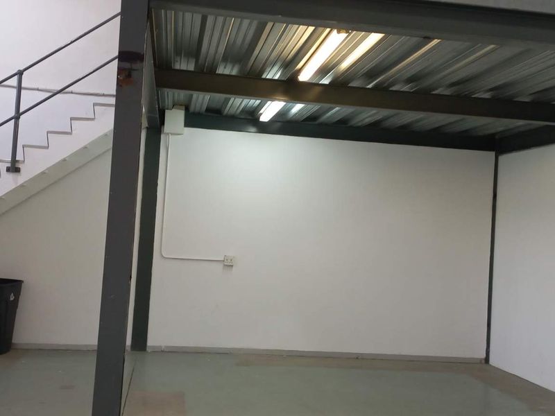 Industrial warehouse space featuring a mezzanine level with steel structure, concrete flooring, and staircase access.