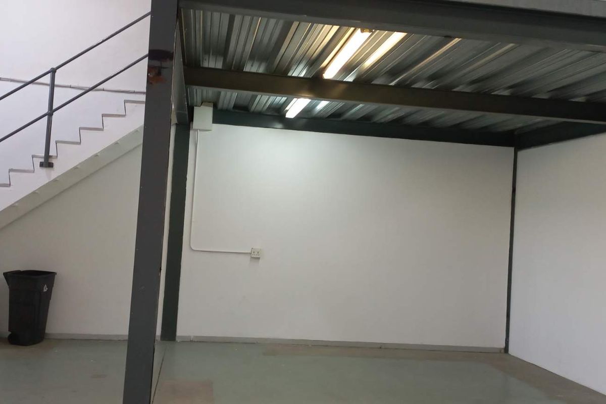 Industrial warehouse space featuring a mezzanine level with steel structure, concrete flooring, and staircase access.