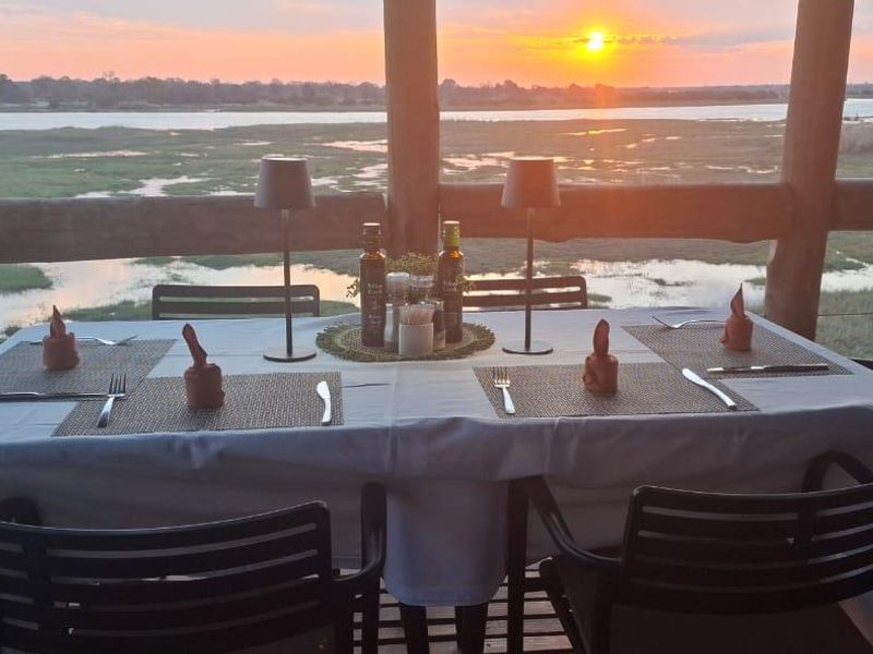 Covered outdoor dining patio featuring timber decking and support posts, offering expansive sunset views over the surrounding landscape and water.