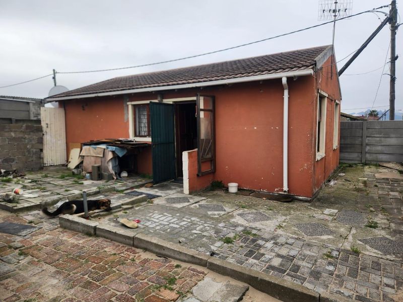 Rear exterior view of a detached house featuring a tiled roof, paved patio area, and concrete boundary walling in need of maintenance.