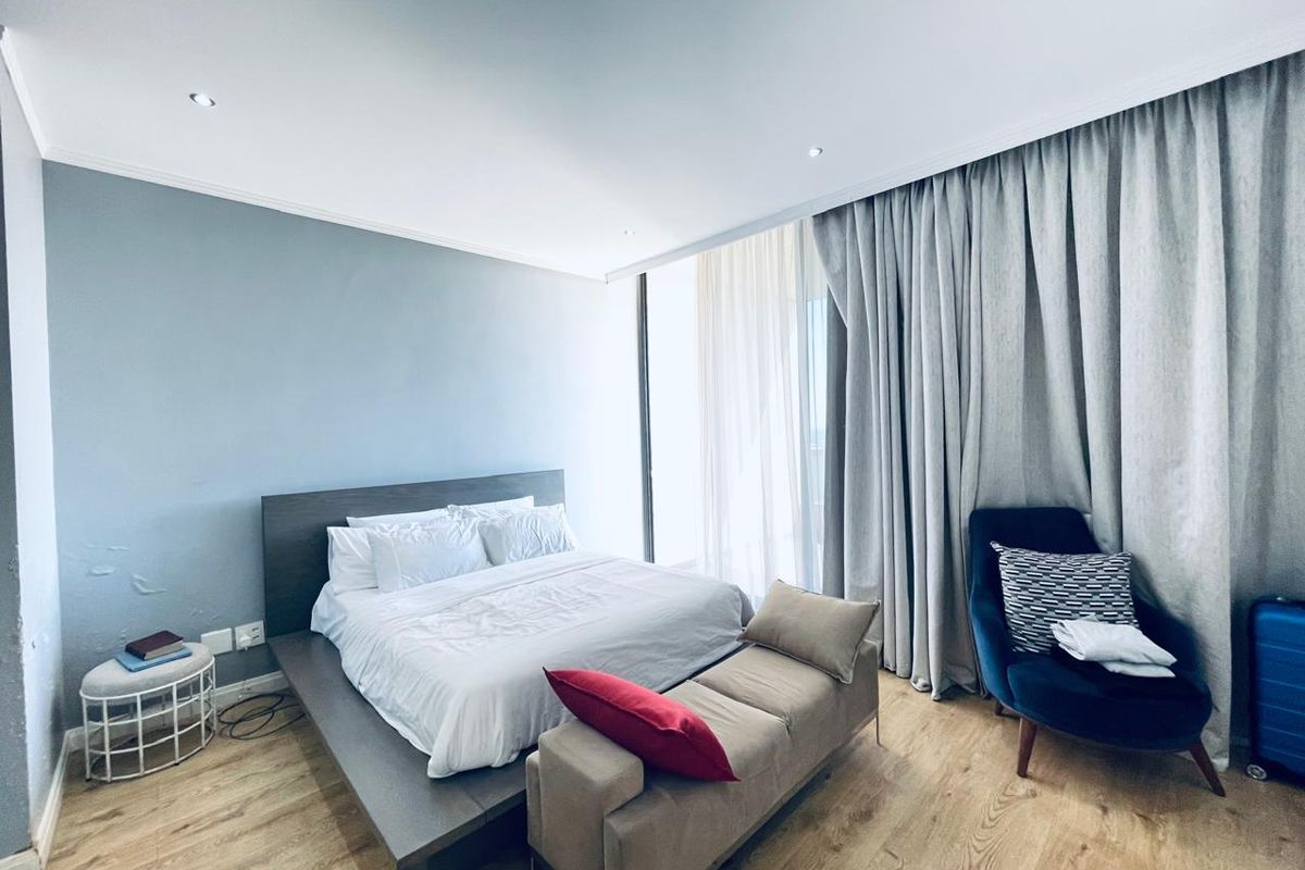 A well-lit bedroom featuring laminate flooring, recessed downlighting, and floor-to-ceiling curtains providing access to natural light.