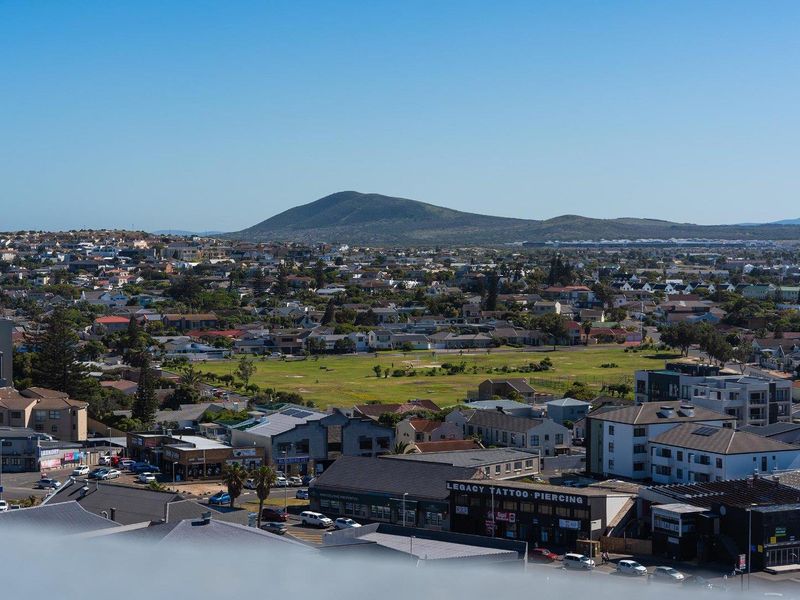 An elevated panoramic view overlooking the surrounding residential neighborhood, local commercial buildings, and distant hills under a clear blue sky.