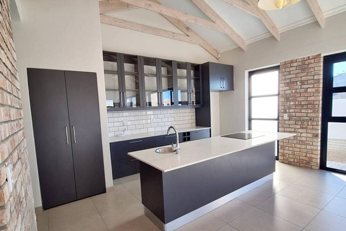 Modern kitchen featuring a central island with stone countertop, dark cabinetry, subway tile backsplash, and exposed timber roof trusses.