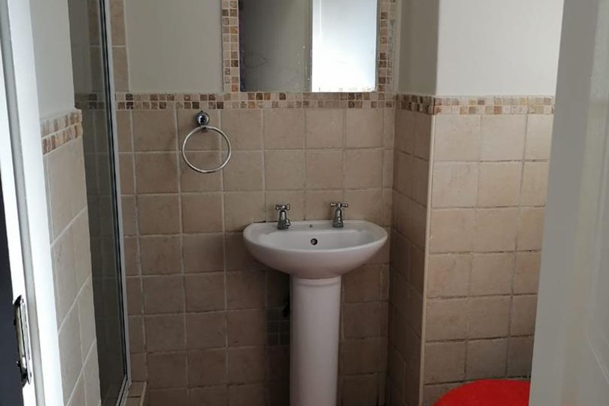A compact bathroom featuring a pedestal basin, a shower enclosure with a glass door, and a toilet, finished with neutral wall and floor tiling.