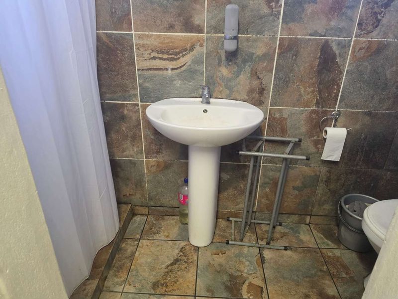 A compact bathroom featuring a pedestal basin, tiled wall and floor finishes, and a shower area with a curtain.