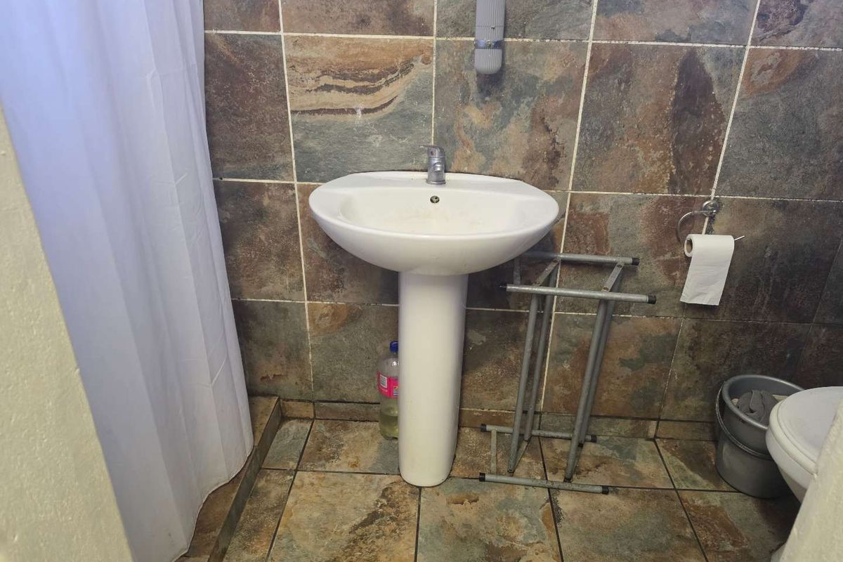 A compact bathroom featuring a pedestal basin, tiled wall and floor finishes, and a shower area with a curtain.