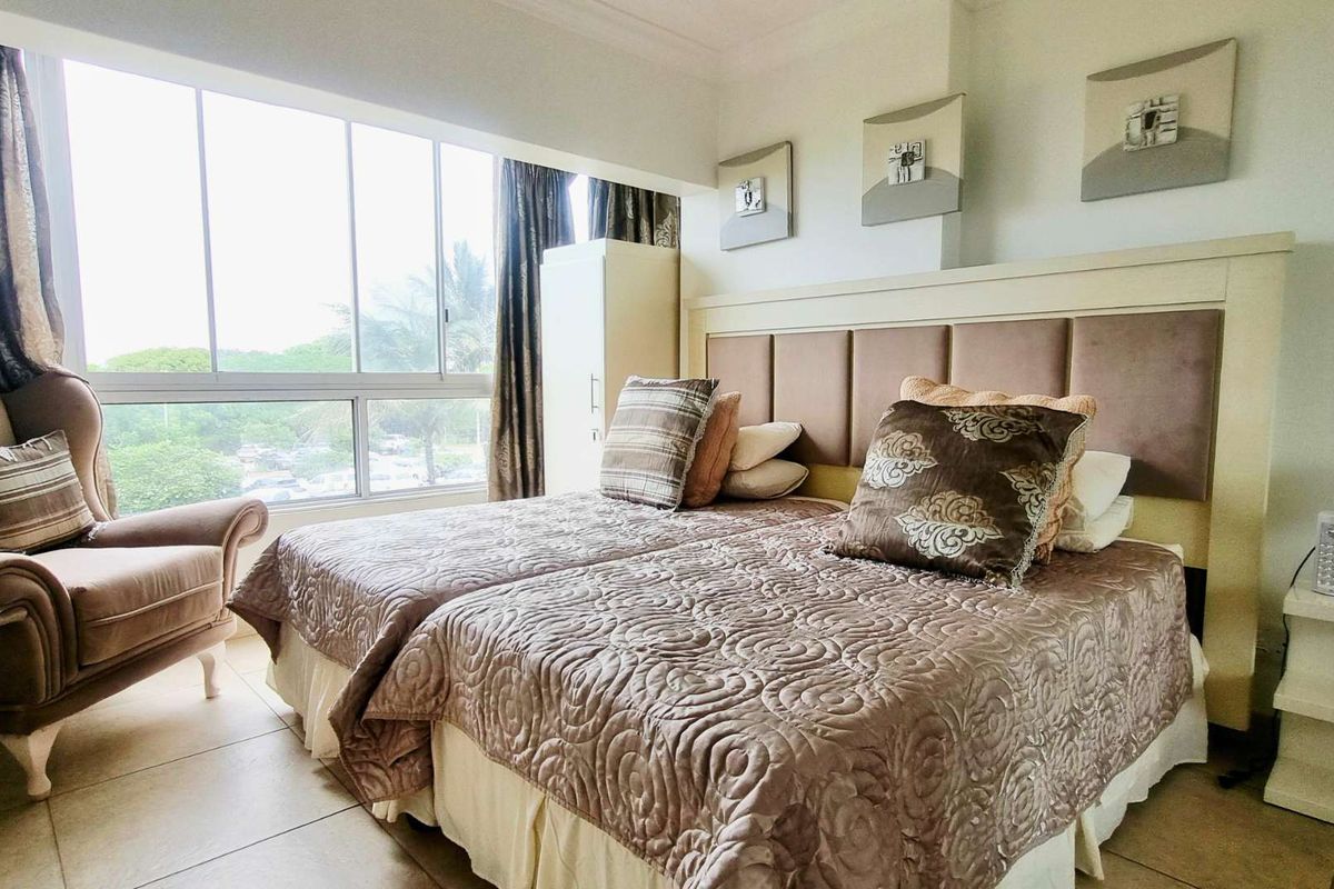 A bedroom featuring large windows with natural light, tiled flooring, and a built-in headboard, offering a comfortable and functional living space.