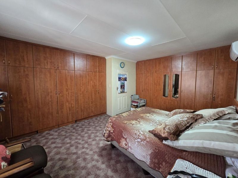 Spacious bedroom featuring extensive wall-to-wall built-in wooden cabinetry, fitted air conditioning, and neutral carpeting.