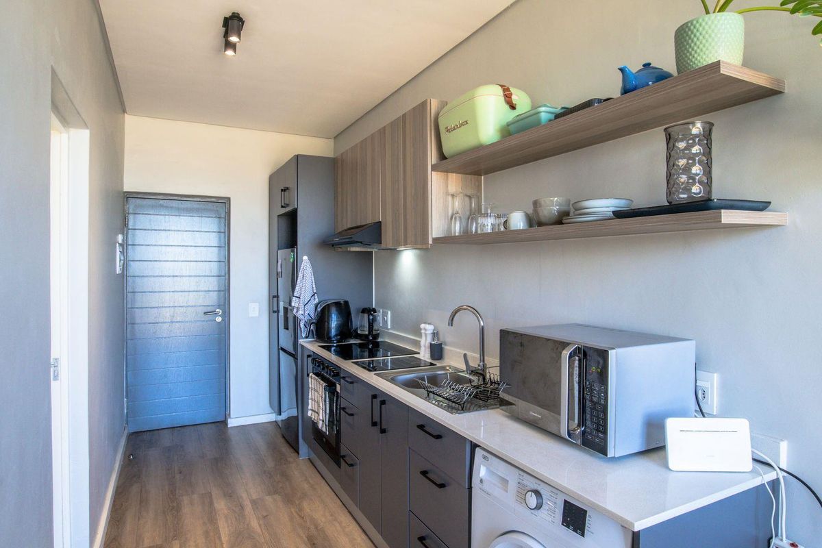 Modern galley-style kitchen featuring sleek grey cabinetry, stone countertops, integrated appliances, and open shelving for a clean, contemporary aesthetic.