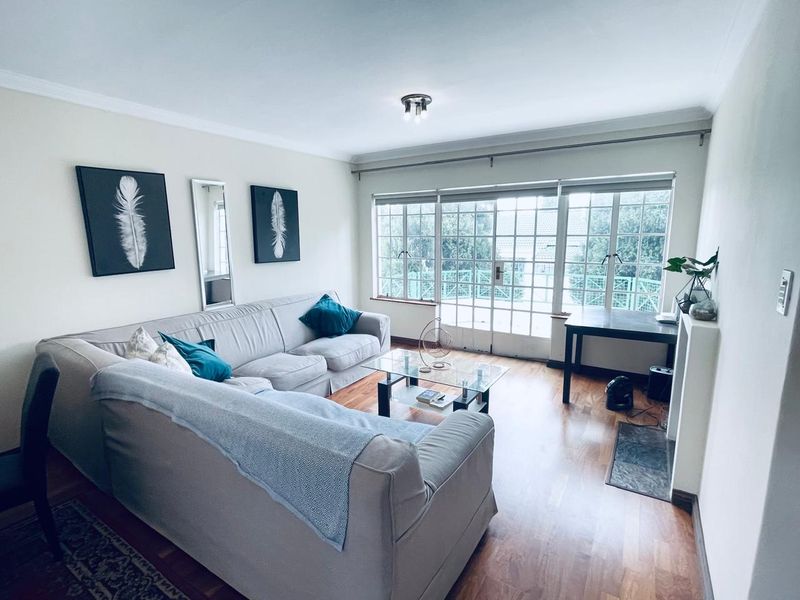 A bright living room featuring laminate flooring, coving, and large french doors that provide ample natural light and access to the exterior.