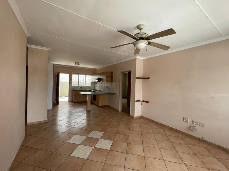 Open-plan living and kitchen area featuring tiled flooring, a ceiling fan, and functional kitchen cabinetry with built-in appliances.