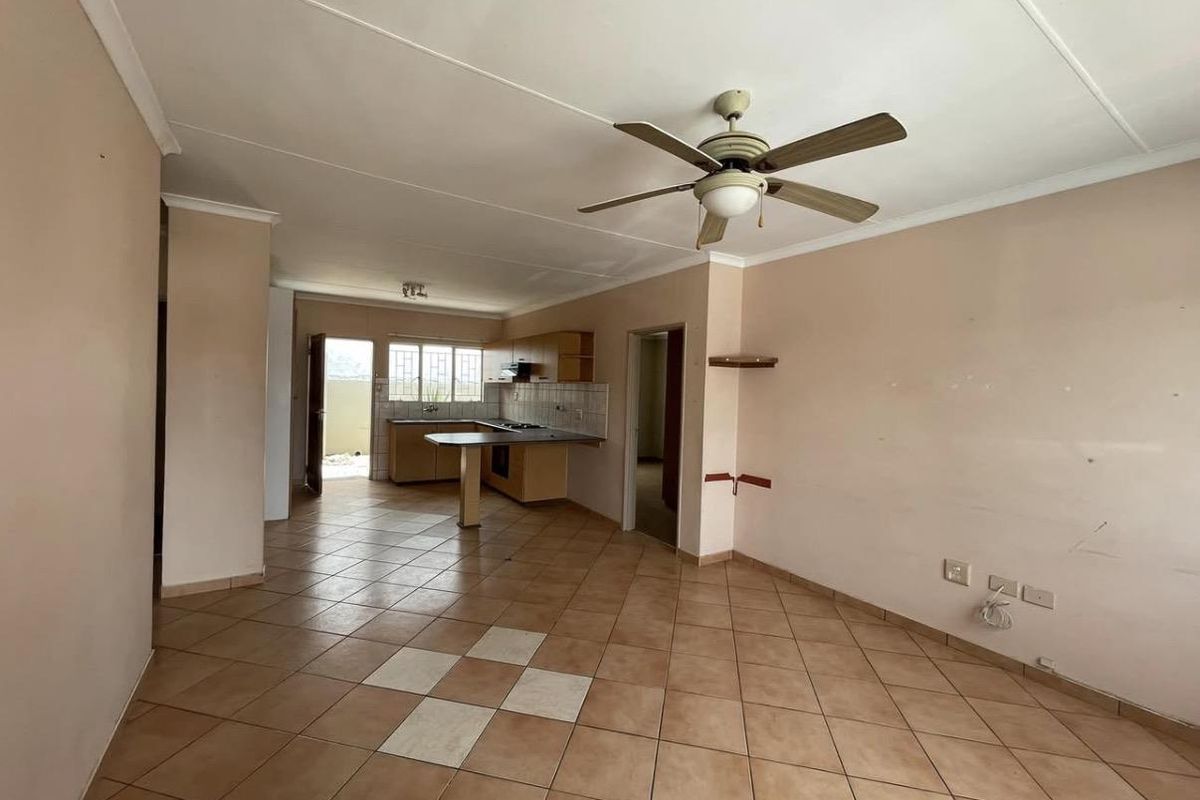 Open-plan living and kitchen area featuring tiled flooring, a ceiling fan, and functional kitchen cabinetry with built-in appliances.