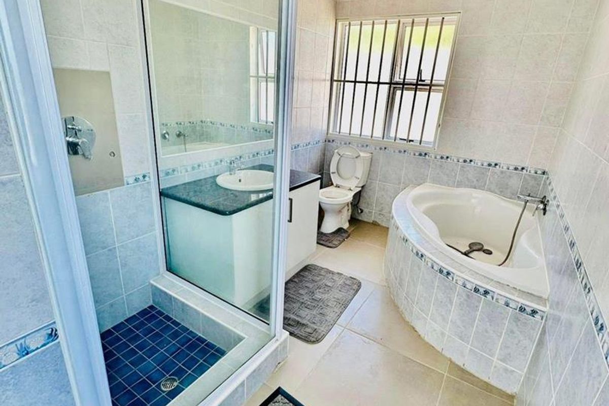 A functional bathroom featuring a glass-enclosed shower, a corner bathtub, a vanity with a basin, and a toilet with security bars on the window.