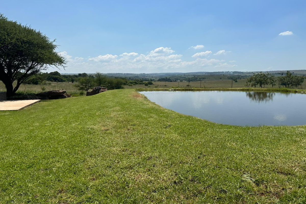 A scenic view of a tranquil farm dam surrounded by lush green lawns and mature trees, showcasing the natural beauty of the agricultural land.