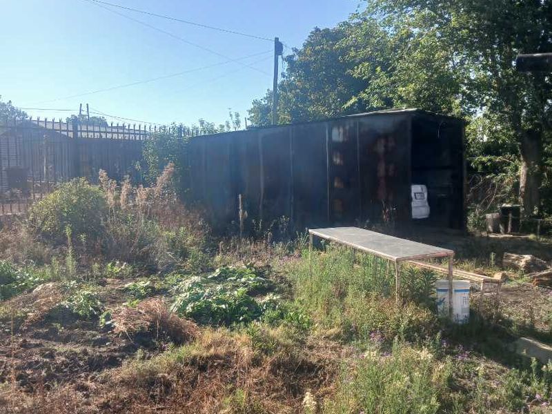 An overgrown garden area featuring a large metal storage container and perimeter fencing, requiring significant landscaping and maintenance.
