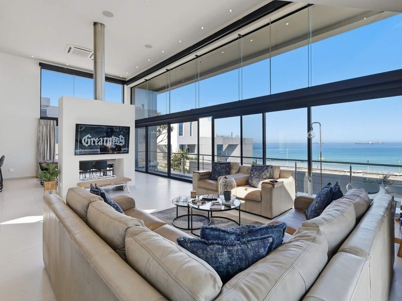 Spacious modern living area featuring floor-to-ceiling glass walls with panoramic ocean views, a central suspended fireplace, and sleek tiled flooring.