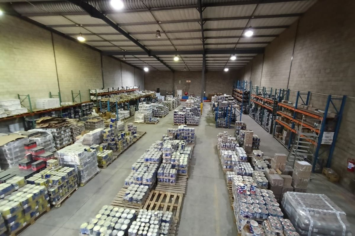Spacious industrial warehouse featuring high ceilings, exposed steel trusses, concrete flooring, and functional high-bay lighting, currently utilized for bulk storage.