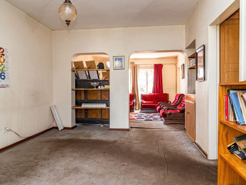 A living room area featuring built-in shelving and an archway leading to an adjacent space, with worn carpeting and dated finishes throughout.
