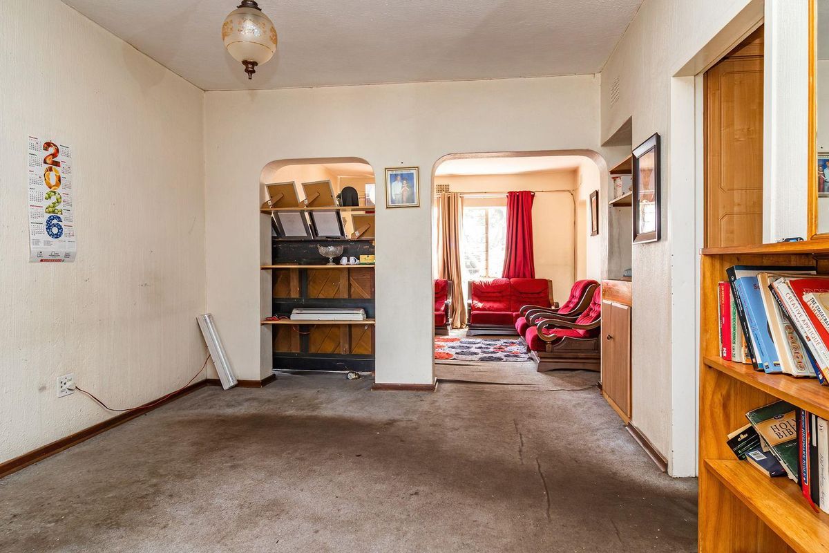 A living room area featuring built-in shelving and an archway leading to an adjacent space, with worn carpeting and dated finishes throughout.