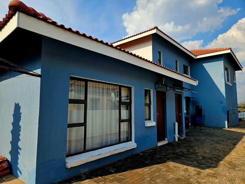 Rear exterior view of the house featuring blue painted walls, terracotta roof tiles, and a paved patio area.
