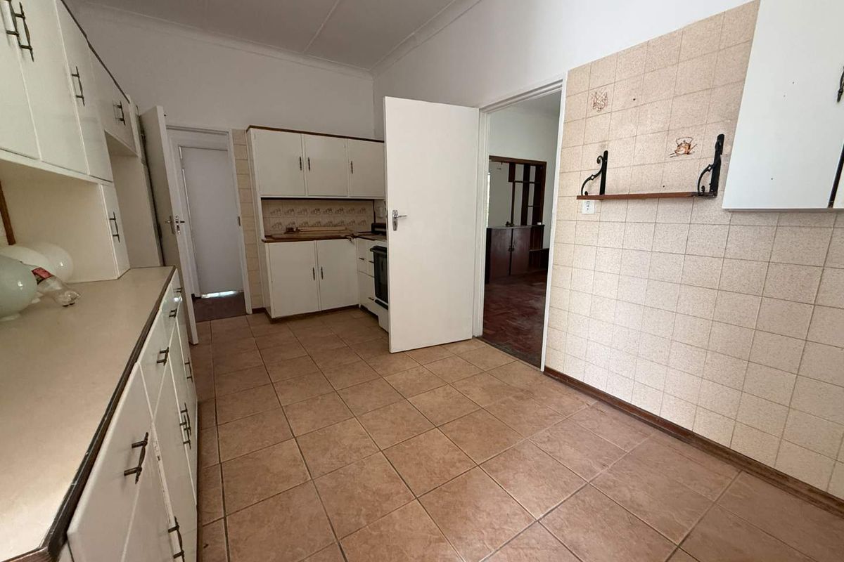 A dated kitchen featuring white cabinetry, tiled flooring, and wall-mounted shelving, offering a functional layout ready for modernization.