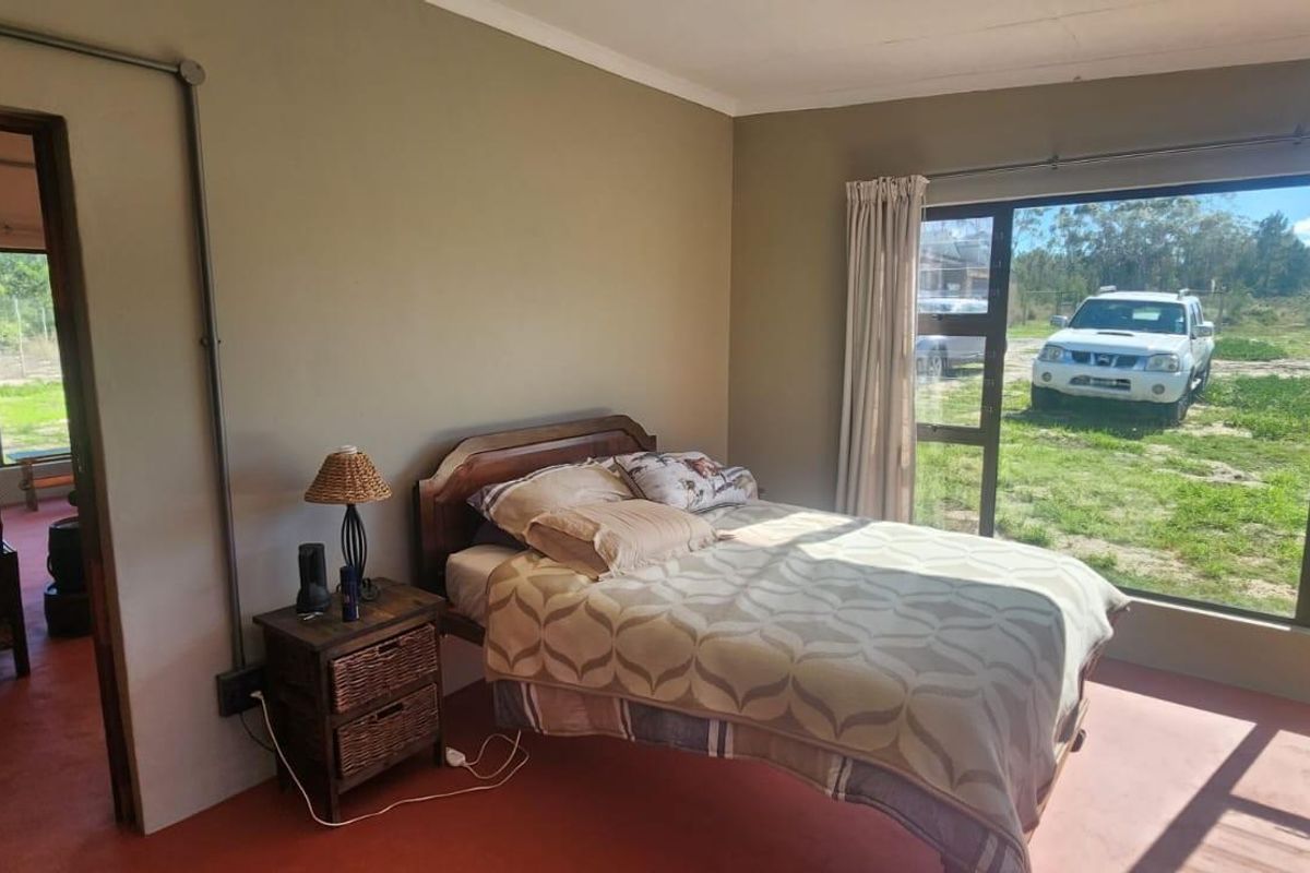 A bedroom featuring large windows with natural light, painted walls, and concrete flooring, offering a view of the surrounding farm landscape.