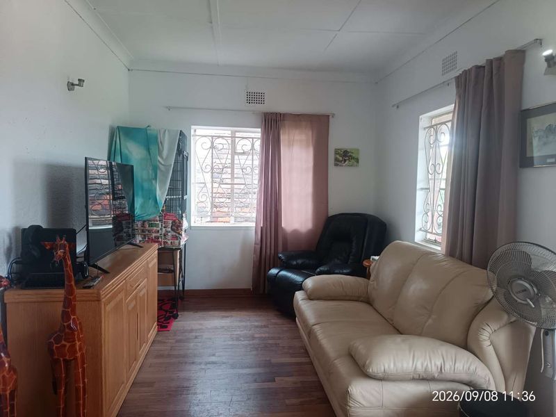 A living room featuring laminate flooring and windows fitted with security bars.