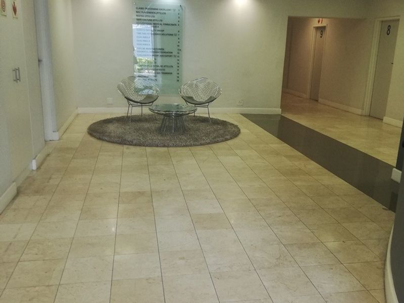 A clean and professional office building entrance lobby featuring tiled flooring, recessed lighting, and a directory board for tenants.