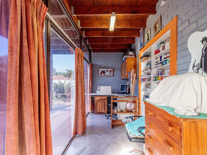 A functional home office featuring exposed timber beams, painted brick walls, built-in shelving, and large sliding glass doors providing access to the patio.
